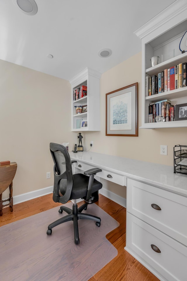 office space with light wood-type flooring, built in shelves, and built in desk