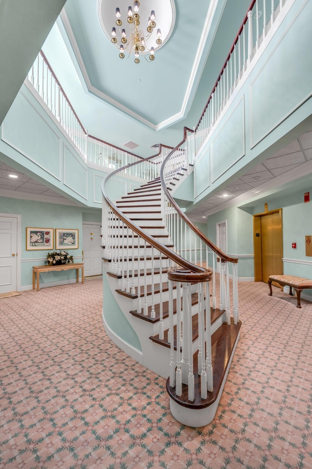 stairway featuring elevator, a notable chandelier, crown molding, a towering ceiling, and carpet