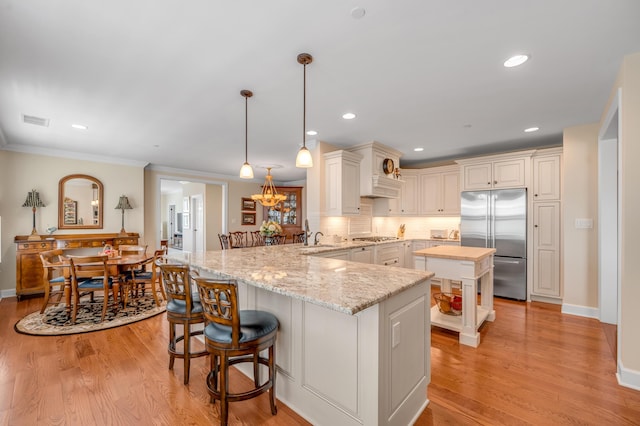 kitchen featuring kitchen peninsula, appliances with stainless steel finishes, a kitchen bar, light stone countertops, and hanging light fixtures