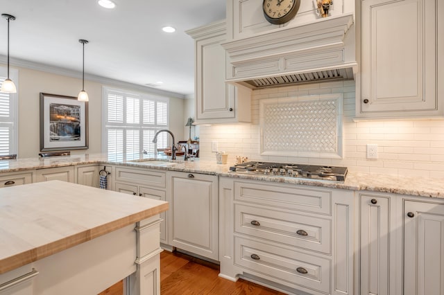 kitchen with sink, backsplash, crown molding, decorative light fixtures, and hardwood / wood-style flooring