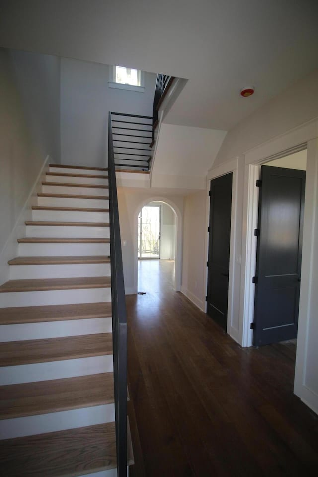 stairs featuring arched walkways, baseboards, and wood finished floors