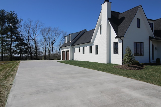 view of side of property featuring a chimney, an attached garage, brick siding, a shingled roof, and a yard