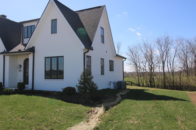 exterior space featuring brick siding, central AC unit, fence, and a lawn