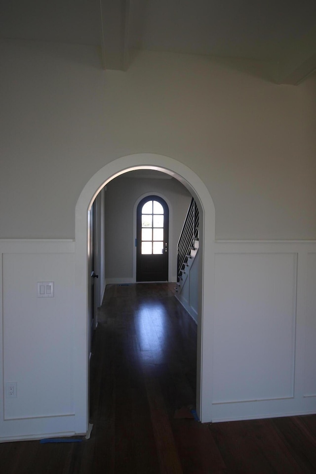 corridor featuring stairway, arched walkways, beam ceiling, dark wood-style floors, and wainscoting