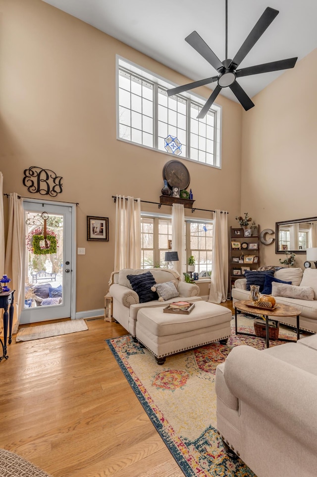 living room featuring ceiling fan, a towering ceiling, and light hardwood / wood-style flooring