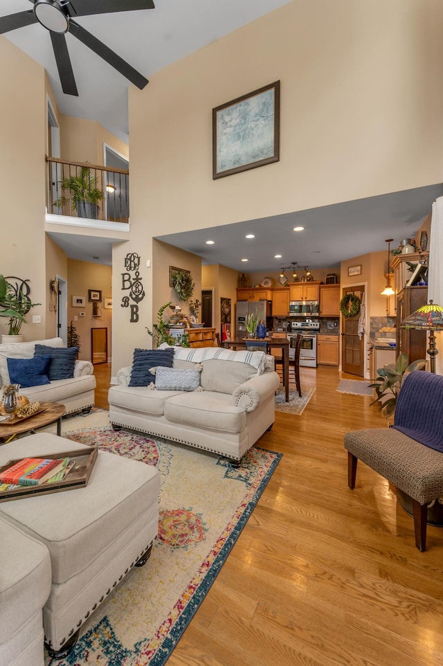 living room with a high ceiling, ceiling fan, and light hardwood / wood-style flooring