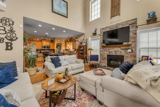 living room featuring a towering ceiling, light hardwood / wood-style flooring, and a stone fireplace