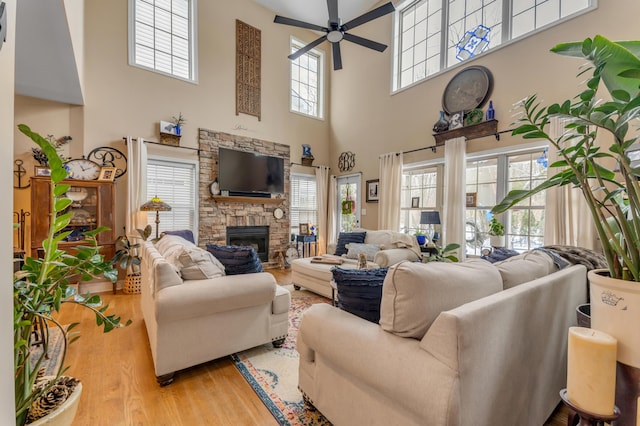 living room featuring ceiling fan, a towering ceiling, a stone fireplace, and light hardwood / wood-style floors