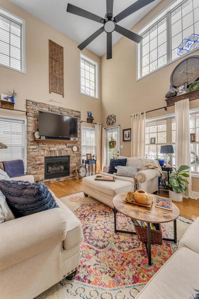 living room featuring a high ceiling, a stone fireplace, a healthy amount of sunlight, and hardwood / wood-style flooring