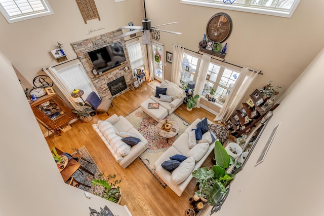 living room featuring ceiling fan, a high ceiling, light hardwood / wood-style flooring, and a fireplace