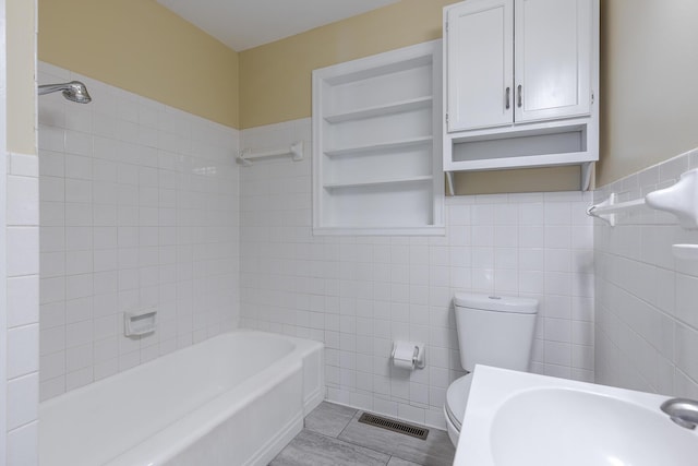 bathroom with tile walls, tiled shower / bath combo, and toilet