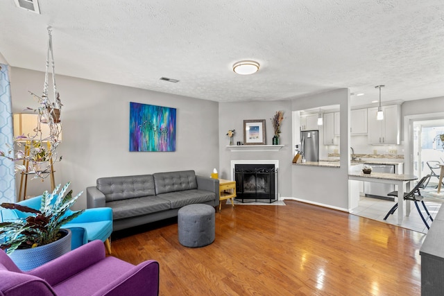 living room with sink, a textured ceiling, and light wood-type flooring