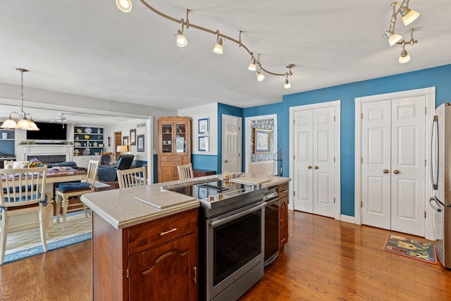 kitchen with appliances with stainless steel finishes, dark hardwood / wood-style floors, a center island with sink, and built in shelves