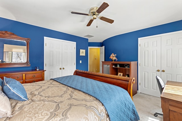 bedroom featuring light carpet, ceiling fan, and two closets