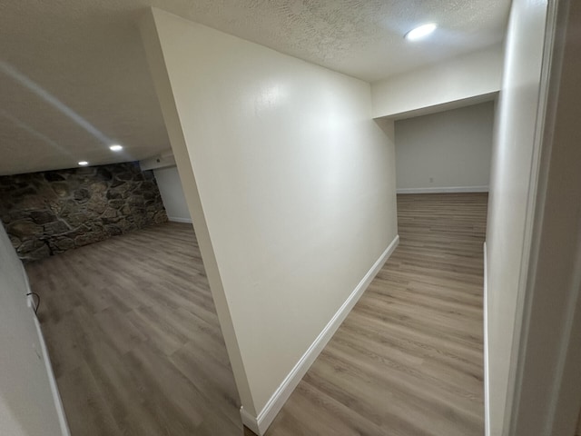 corridor with a textured ceiling and light hardwood / wood-style floors