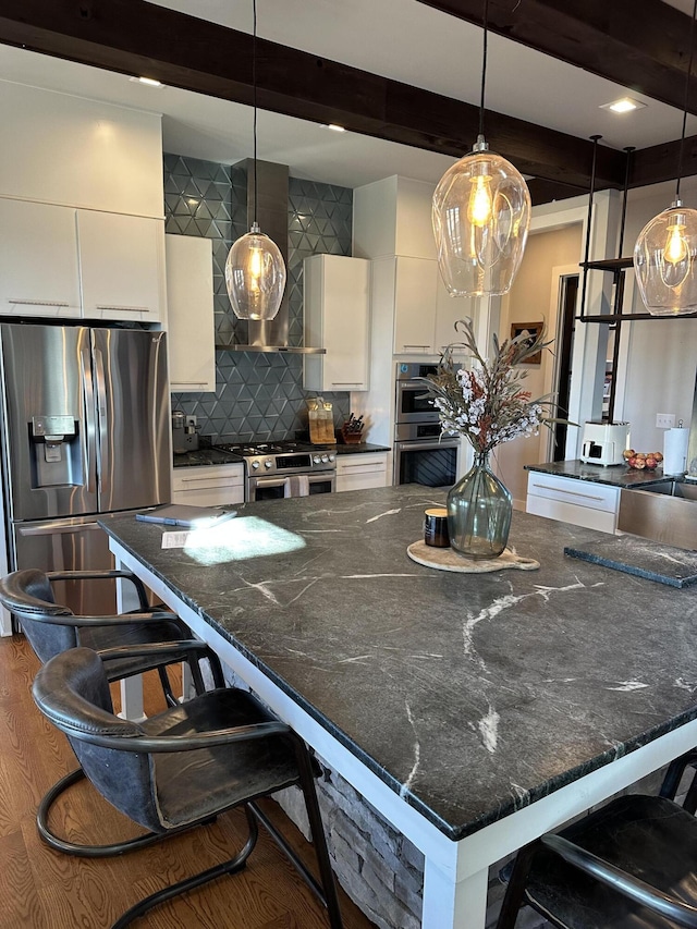 kitchen featuring decorative light fixtures, white cabinets, a kitchen breakfast bar, stainless steel appliances, and wall chimney range hood