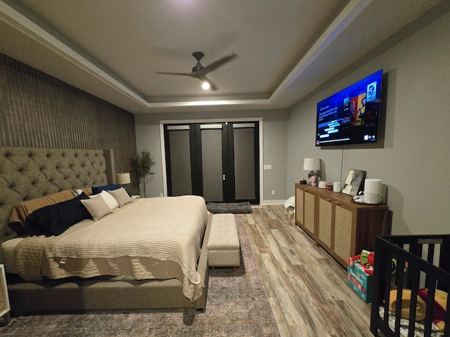 bedroom with hardwood / wood-style flooring, ceiling fan, and a tray ceiling