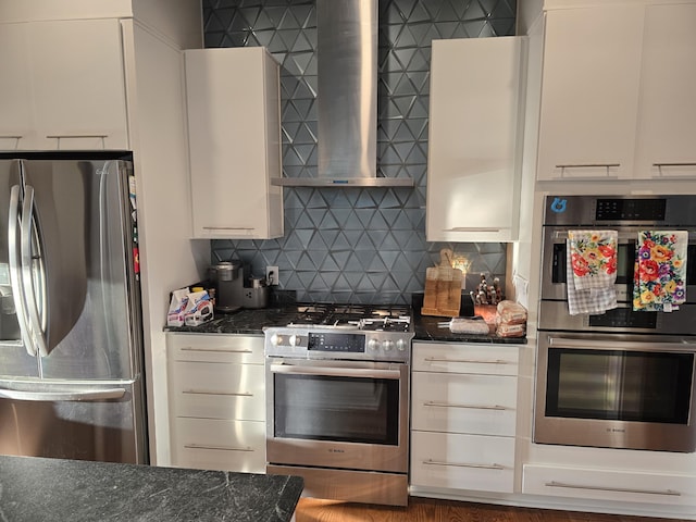 kitchen with wall chimney range hood, dark stone counters, and appliances with stainless steel finishes