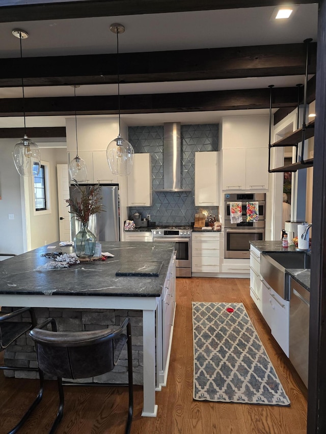 kitchen featuring pendant lighting, wall chimney range hood, white cabinetry, and stainless steel appliances