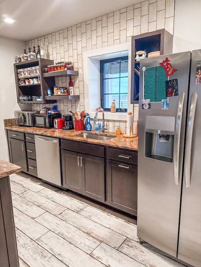 kitchen with stainless steel appliances, sink, dark brown cabinetry, and dark stone counters