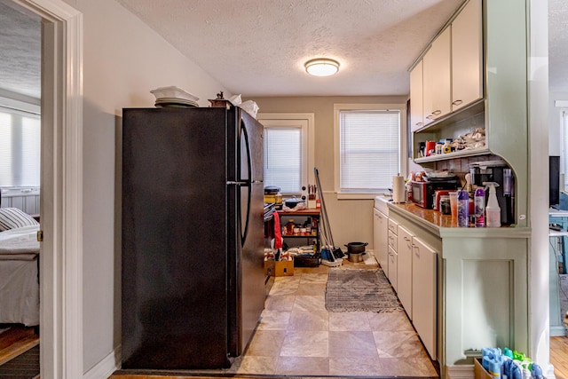 kitchen featuring black fridge, a textured ceiling, plenty of natural light, and white cabinetry