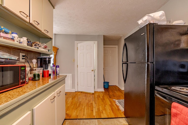 kitchen featuring black fridge, a textured ceiling, light wood-type flooring, and white cabinetry