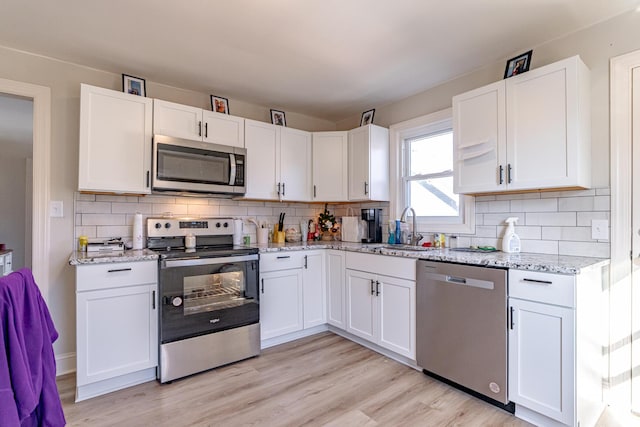 kitchen featuring stainless steel appliances, white cabinets, sink, and light stone counters