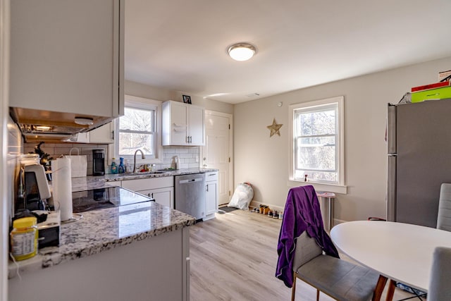 kitchen with stainless steel appliances, sink, white cabinetry, light stone counters, and decorative backsplash