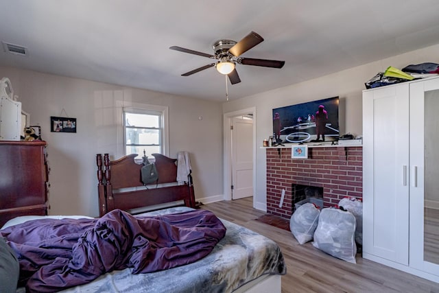 bedroom featuring a fireplace, ceiling fan, and light hardwood / wood-style flooring