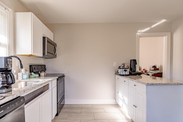 kitchen with stainless steel appliances, kitchen peninsula, light stone countertops, sink, and white cabinetry