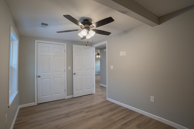 unfurnished bedroom with beam ceiling, ceiling fan, light hardwood / wood-style flooring, and a closet