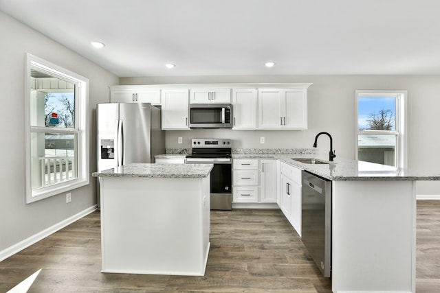 kitchen with appliances with stainless steel finishes, white cabinetry, light stone counters, and sink