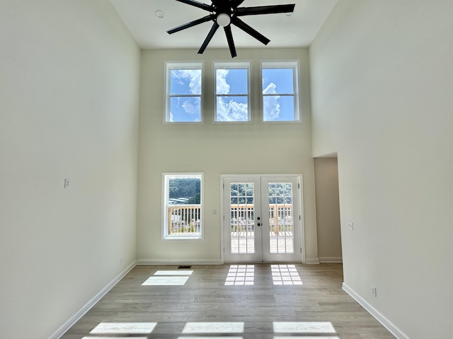 unfurnished living room with a towering ceiling, french doors, ceiling fan, and light wood-type flooring