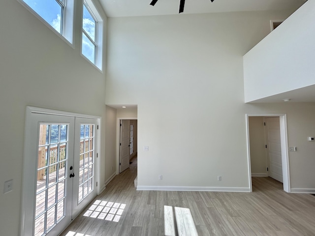 unfurnished living room featuring a towering ceiling, ceiling fan, french doors, and light hardwood / wood-style floors