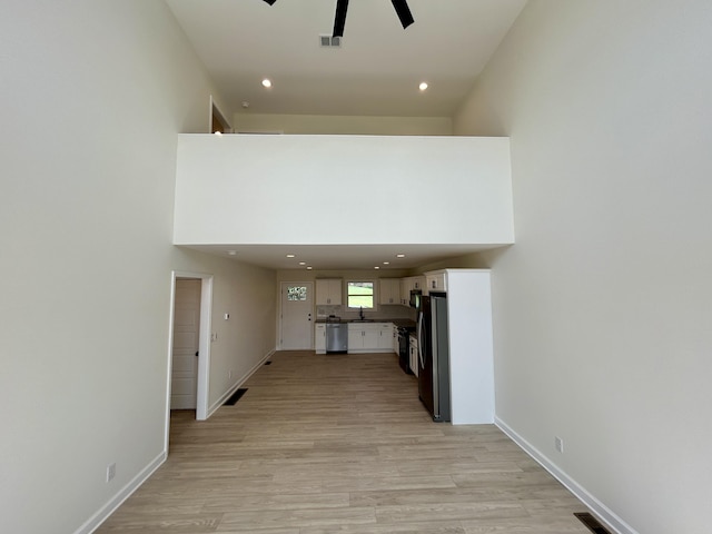 hall with sink, a high ceiling, and light wood-type flooring