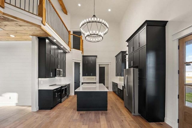 kitchen with a center island, an inviting chandelier, a high ceiling, hanging light fixtures, and appliances with stainless steel finishes