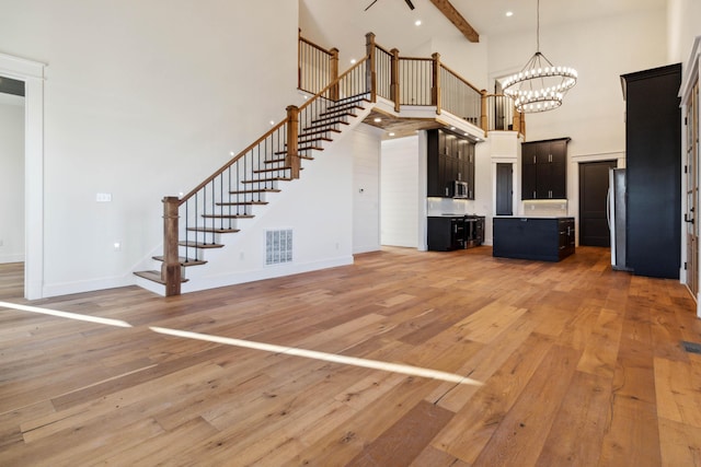 unfurnished living room featuring wood-type flooring, a notable chandelier, beamed ceiling, and a high ceiling