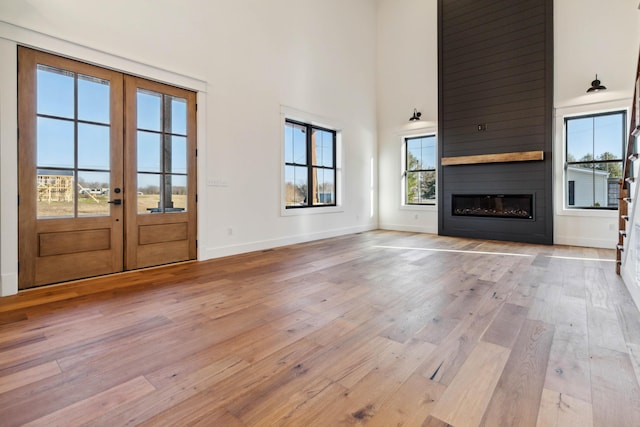 unfurnished living room with light hardwood / wood-style floors, a high ceiling, a large fireplace, and french doors