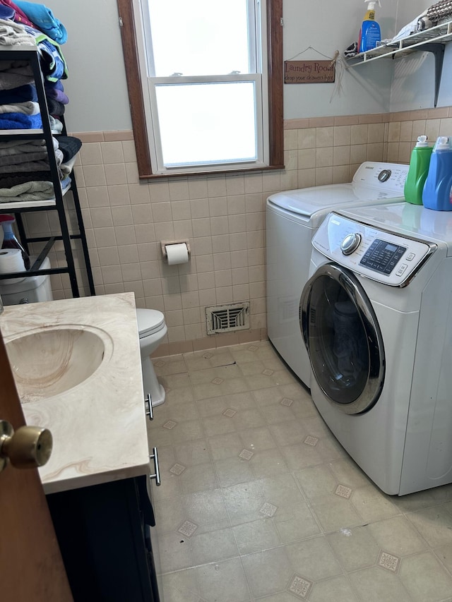 washroom featuring sink, tile walls, and washing machine and clothes dryer