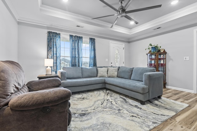 living room with ornamental molding, a raised ceiling, ceiling fan, and light wood-type flooring