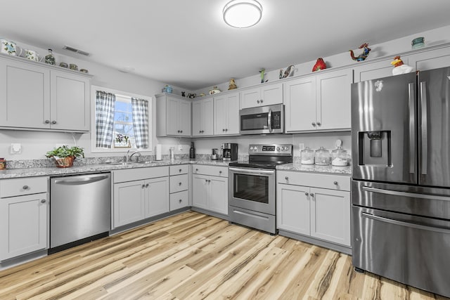 kitchen with light stone countertops, light hardwood / wood-style flooring, stainless steel appliances, and sink