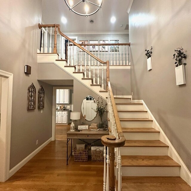 stairs featuring a high ceiling, crown molding, and hardwood / wood-style floors