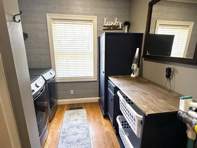 kitchen with electric range oven, plenty of natural light, light wood-type flooring, and wooden walls