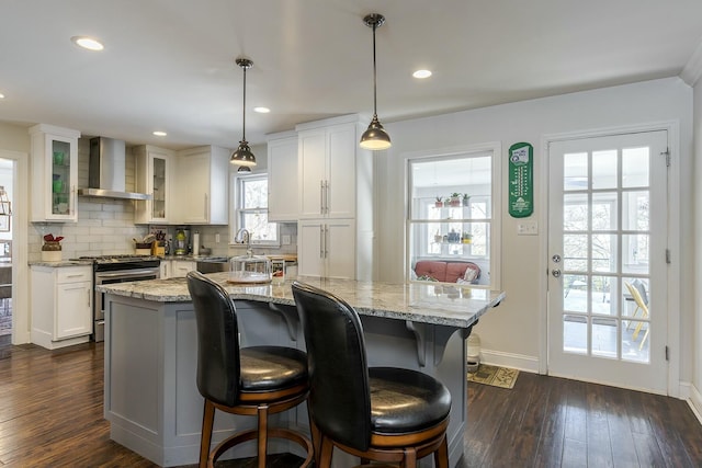 kitchen featuring a center island, wall chimney exhaust hood, white cabinets, stainless steel range oven, and decorative light fixtures