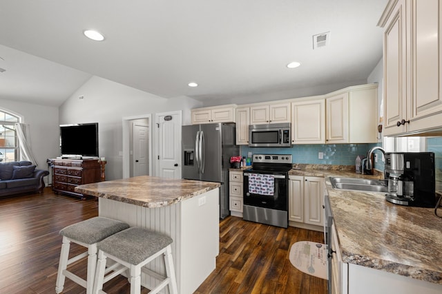 kitchen with appliances with stainless steel finishes, a kitchen island, a kitchen bar, decorative backsplash, and vaulted ceiling