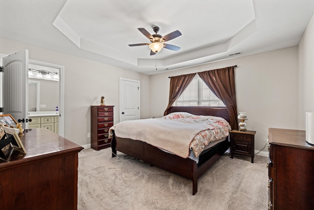 carpeted bedroom featuring ceiling fan, a tray ceiling, and ensuite bathroom