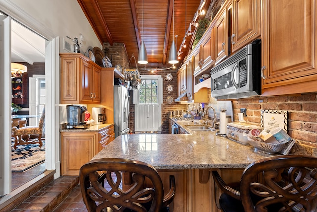 kitchen with appliances with stainless steel finishes, beamed ceiling, kitchen peninsula, sink, and backsplash