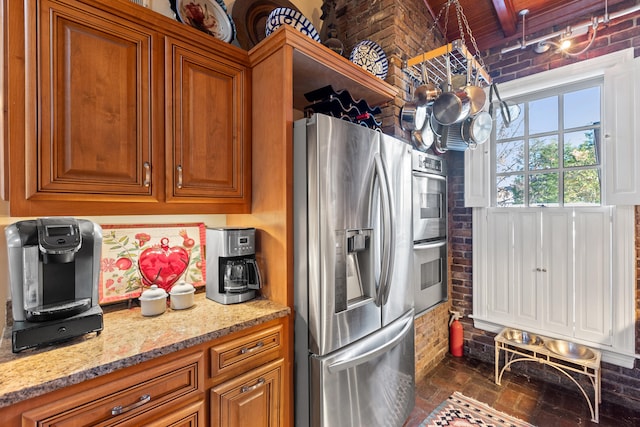 kitchen featuring light stone countertops, brick wall, appliances with stainless steel finishes, and beamed ceiling