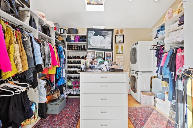 walk in closet with stacked washer / drying machine, light wood-type flooring, and vaulted ceiling with skylight