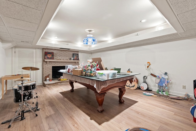 recreation room featuring a fireplace, light wood-type flooring, and a raised ceiling